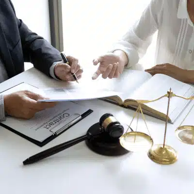 Two people discuss legal documents and contracts with a gavel and scales on the desk