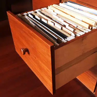 Open wooden filing cabinet drawer showing folders, used for retrieval of records in an office