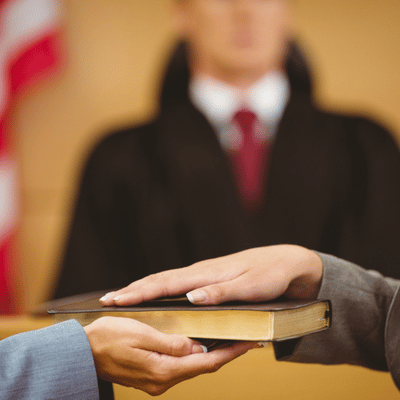 A witness places hand on a Bible, swearing an oath in front of a judge
