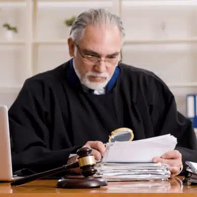 Judge studies case files with magnifying glass at desk; gavel nearby indicates formal legal review