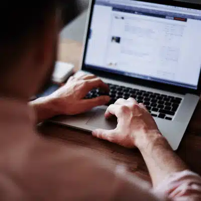 Man works on laptop at home, browsing documents and emails in dim evening light alone