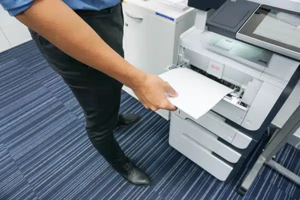 Employee retrieves printed page from office laser printer, checking tray alignment and paper handling today