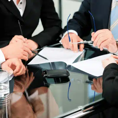 Executives point at documents during agreement talk in war meeting room with pens ready