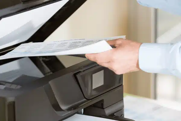Hand feeds document into office copier for legal photocopy service, producing clean copies of forms