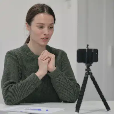 Woman speaks to smartphone on tripod, Video production for attorneys, preparing testimony notes at table