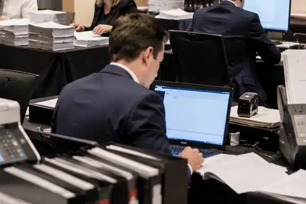 A legal professional works on a laptop surrounded by printers, binders, and document stacks while legal copy services in marshall tx support trial preparation